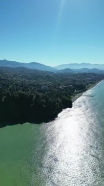 Batumi Botanik Bahçesi yakınlarındaki Karadeniz kıyısı. Dikey 4K drone görüntüleri yemyeşil yemyeşil, kıyı kayalıkları ve açık güneşli havada açık mavi deniz manzaraları gösteriyor..