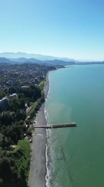 Batumi Botanik Bahçesi yakınlarındaki Karadeniz kıyısı. Dikey 4K drone görüntüleri yemyeşil yemyeşil, kıyı kayalıkları ve açık güneşli havada açık mavi deniz manzaraları gösteriyor..