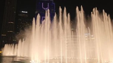Dubai, BAE. 3 Ekim 2024. Gece gölünde ünlü Dubai Çeşmesi gösterisi, popüler turistik cazibe, insan yapımı sihirli sanat eseri güzellik, aydınlatılmış su dansı. Arkaplan Arap şehrinde inanılmaz uzun mimari