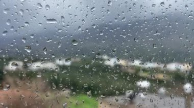 Bulanık yeşil manzaralı pencere camında yağmur damlaları ve kasvetli bir sonbahar fırtınasında veya yağmurlu bir günde arka planda dağlar