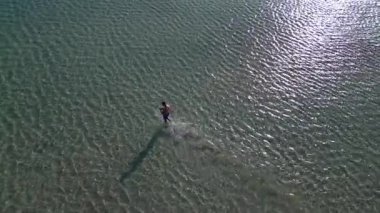 İHA atışı: şortlu bir adam sığ turkuaz deniz suyunda yürüyor güneş dalgaları, Elafonisi plajı, Girit