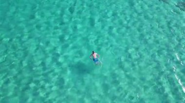 Girit adasındaki Elafonisi sahilinde ağırlıksız bir şekilde yüzen rahat bir yüzücünün ferah ve ferah sularla çevrili halinin insansız hava aracı görüntüsü..