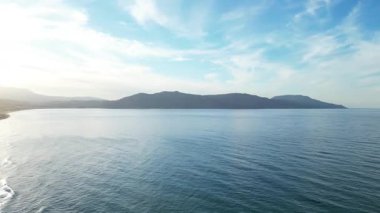 İHA hava aracı: Geniş mavi Akdeniz manzarası, yumuşak bulutlu gökyüzü altında uzak karanlık dağ siluetleri