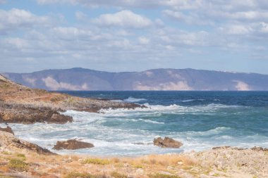 Kayalara çarpan güçlü sörfler, beyaz köpüklü ve berrak gökyüzüyle zümrüt mavisi deniz, hareket, güç ve doğal enerjiyle dolu dinamik dramatik manzara.