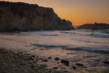 Kayalık çakıl taşlı plaj ön planında yumuşak okyanus dalgaları altın saat boyunca devasa uçurumlara yaklaşıyor. grafik tasarımı için seyahat ve doğal deniz kenarı arkaplan dokusu.