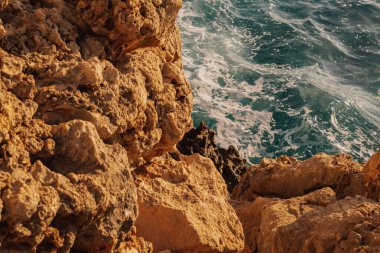 Kayalık kıyı şeridine yakın bir yerde kıyı aşınması ve derin mavi Akdeniz suları görülüyor. Jeolojiyi, hava durumunu ve el değmemiş doğayı vurgulayan doğal bir manzara..