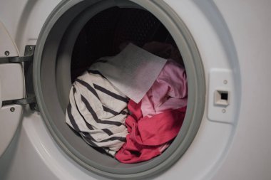 Çamaşırları korumak için renkli çarşaflarla dolu renkli çamaşır makinesini aç. Boya kanamasının ve kumaş hasarının önlenmesi gereğini vurgulayan ev işi kavramı.