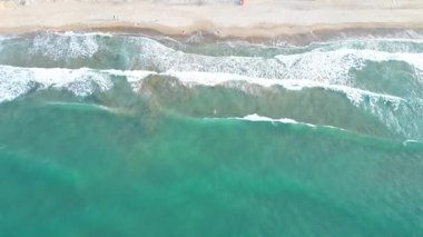Üst görüntü insansız hava aracı görüntüleri: güçlü turkuaz dalgalar Girit kıyısında beyaz köpükle çarpışıyor, fırtınalı Akdeniz sularında yüzen cesur genç kadın, sinematik hava dalgaları