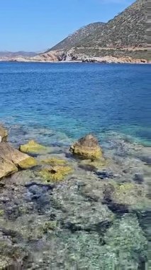 Dikey çekim: Girit adasında kayalık akdeniz yatağı üzerinde kristal berrak turkuaz su, şeffaf dalgalar aracılığıyla kayalara yansıyan güneş ışığı, Yunan kıyıları