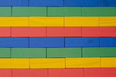 Parlak renkli tahta oyuncak bloklarından (kırmızı, sarı, yeşil ve mavi) yapılmış bir duvarın yakın planı düzenli bir geometrik desen ve doku ile düzenlenmiştir.