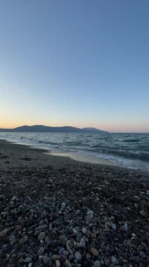 Sakin bir Girit çakıl taşı sahili alacakaranlık manzarası, yumuşak akşam renkleriyle, sakin karanlık su, ve sakin bir kıyı havası yaratan açık bir eğimli gökyüzü. Girit adasında rahatla. Yüksek kalite 4k görüntü