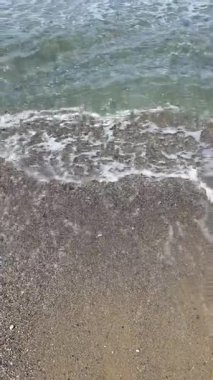 Dikey yakın çekim: beyaz köpüklü deniz dalgaları kumlu çakıl taşlı plajları, berrak Akdeniz suları