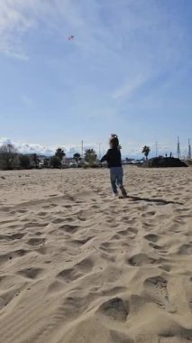 Plajda renkli bir uçurtmayla koşan küçük bir kız. Yunanistan 'da Temiz Pazartesi' yi mavi bir ufukta kutluyoruz. Neşeli çocukluk özgürlüğü ve bahar tatili yaşam tarzı. Yüksek kaliteli FullHD görüntüler