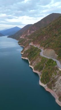 Zhinvali Reservoir boyunca dönen bir dağ yolunun dikey drone görüntüsü. S- eğri asfalt yolu yemyeşil ormanlarda ve turkuaz sularda. Manzaralı Gürcü araba gezisi. Yüksek kalite 4k görüntü