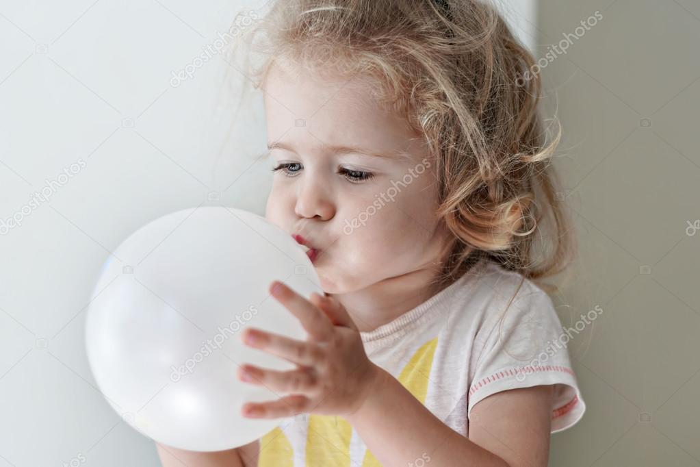 Adorable child girl is inflating a white balloon at the light room close-up