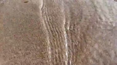 Islak kumsalda akan deniz suyunun soyut yakın çekimi