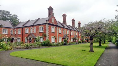 Sessiz bir İngiliz yerleşim bölgesinde bulutlu bir günde tarihi kırmızı tuğlalı evler süslü bacaları ve çatıları olan manikürlü bir bahçe yolu çiziyor.