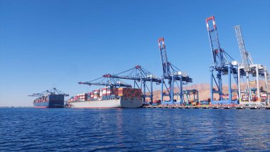 Kargo gemileri ticari bir nakliye limanına yanaştı. Geniş vinçler açık bir gökyüzünün altındaki konteynırları yükleyip boşaltarak küresel ticaret operasyonlarını ve denizcilik lojistiğini vurguluyor..