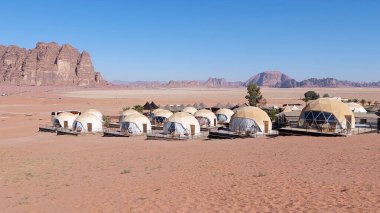 Ürdün 'ün Wadi Rum kentindeki engebeli kumtaşı dağlarına kurulmuş berrak mavi gökyüzü altında bir çöl beldesindeki fütüristik kubbe çadırları eşsiz ve manzaralı bir geri çekilme deneyimi sunuyor.