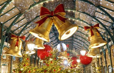 Noel süslemeleriyle süslenmiş kapalı bir oyun salonu ya da kapalı bir pazar. Kemerli metal tavandan sarkan kırmızı fiyonklu büyük altın çanlar içeriden aydınlatılıyor ve sıcak bir parıltı yaratıyor. Tavan ışıldıyor.