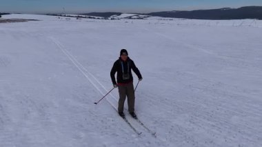 Yetişkin bir insan kış aylarında geniş bir kar tarlasında kayaklarla koşar. Bakımsız bir patikada kayak direklerini kullanır. Gökyüzü altında bir dron kullanarak yukarıdan çekilen bir video..