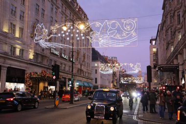 Londra, Birleşik Krallık - 30 Aralık 2025: Londra 'da gece karanlığında siyah bir taksi ve kaldırımda yürüyen bir kalabalık. Sokaklar Noel ışıklarıyla aydınlandı..