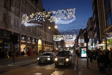 Londra, Birleşik Krallık - 30 Aralık 2025: Londra 'da gece karanlığında siyah bir taksi ve kaldırımda yürüyen bir kalabalık. Sokaklar Noel ışıklarıyla aydınlandı..