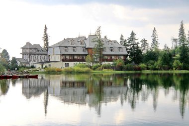 Strbske pleso, Slovakya - 05 Eylül 2014: Geleneksel kereste mimarisine sahip Lakeside oteli, Strbske pleso gölünün sakin sularına yansıyarak, yumuşak gün ışığında yeşil ağaçlar ve yeşilliklerle çevrelenerek, sakin bir kırsal alan inzivası yarattı.