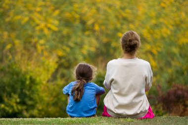 Anne ve oğul sonbaharda ağaçların sarı yapraklarına bakıyor.