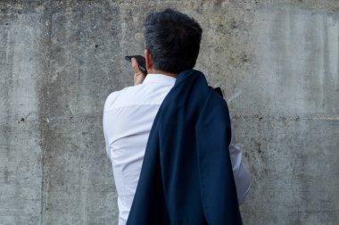 Beton duvardaki cep telefonuna bakarken akıllı telefondan fotoğraf çeken işadamının arka görüntüsü