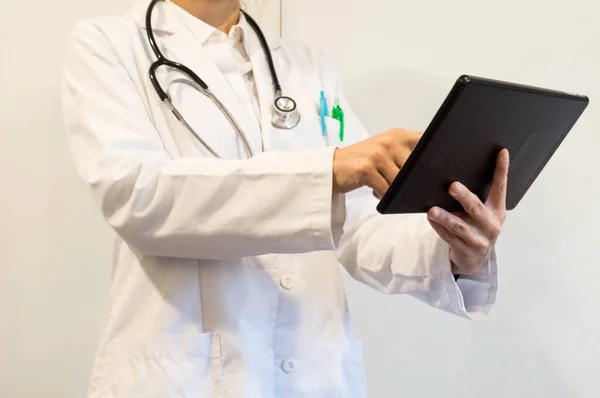 Beyaz üniformalı doktor elinde bir tablet tutuyor.
