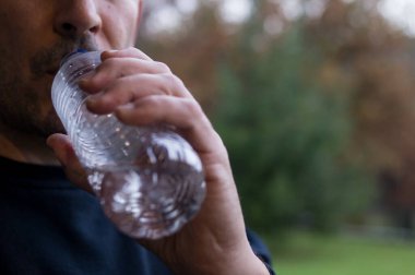Açık havada plastik bir su şişesinden içen adam mikro plastik yutmayı ve ambalajdan kimyasal maruz kalmayı sembolize ediyor..
