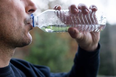 Açık havada plastik bir su şişesinden içen adam mikro plastik yutmayı ve ambalajdan kimyasal maruz kalmayı sembolize ediyor.