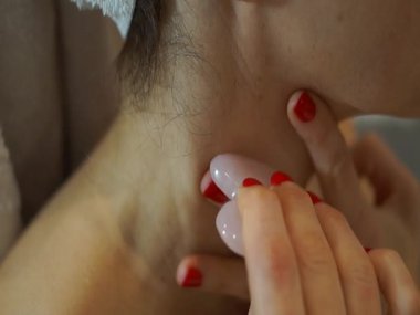 Ensesine masaj yapmak için cilalı bir mineral taşı (Gua Sha) ve lenfatik drenaj ve kas gerilimi için çene hattı kullanan bir kadının yakın çekimi.