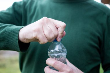 Elleri yakın plan temiz bir plastik su şişesini açıyor. Sıvıların içine sızan bir mikroplastik kaynağı..