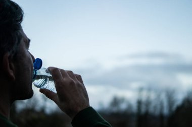 Doğrudan plastik şişeden su içen bir adamın profil görüntüsü, birincil mikroplastik yutma kaynağı..