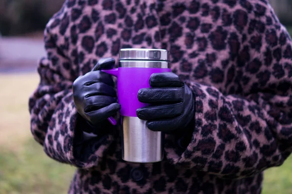 Elinde mor ve paslanmaz çelikten bir şişe tutan siyah eldivenli ellerin ön görüntüsü, malzemelere odaklanmış..