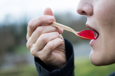 Parlak kırmızı jöle yiyen, işlenmiş gıda tüketimini, yapay katkı maddelerini ve kimyasal maddeleri sembolize eden bir kişinin yakın çekimi. Anahtar sözcükler: yemek, jelatin, jöle, tatlı, kaşık,