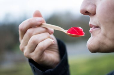 Bir kaşık dolusu kırmızı jelatin yemek üzere olan birinin profili, sentetik doku ve renklerin diyete nasıl entegre olduğunu gösteriyor..