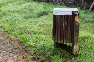 Yeşil çimen tarlasında duran ve parkın bakımını vurgulayan, plastik kaplamalı, kırsal ahşap bir çöp konteynırı..