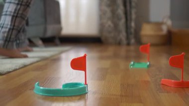 Pijamalı bir adam ahşap bir zeminde renkli plastik bir golf setiyle atış becerilerini geliştiriyor. Ev içi boş zamanlara ve ev sporlarına odaklanıyor..