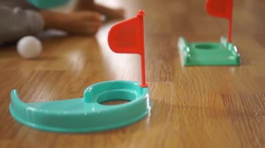 Detaylı bir çekimde bir çocuk plastik turkuaz bir sopayla kırmızı bayrakla beyaz bir topa vururken görülüyor. Kapalı alanda oyun ve motor becerileri gelişimi kutlanıyor..