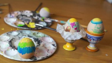 Güzel dekore edilmiş bir Paskalya yumurtası. Pembe bir tavşancık ve yeşil çimenler var. Seramik bir fincanda diğer boyalı yumurta ve sanatçı paletlerinin yanında..