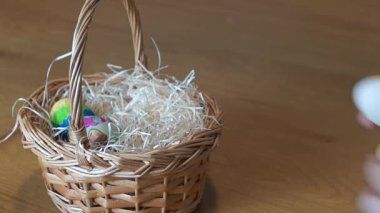 İki el dikkatle birçok parlak renkli ve dekore edilmiş Paskalya yumurtalarını samanla bir sepete yerleştirerek, şenlikli bir gösteriye veya hediyeye hazırlanıyor..