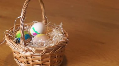 Bir çocuğun eli dikkatlice boyanmış bir Paskalya yumurtasını samanla dolu geleneksel bir hasır sepete yerleştirirken. Tahta yüzeyde yumuşak doğal aydınlatma.