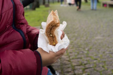 Bir çocuk, peçeteyle sandviçi dikkatlice tutarken, aileler için basit ve besleyici sokak yemekleri sunar.