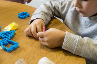 Solak bir gencin yakın plan fotoğrafı. Ahşap bir masa üzerindeki renkli kil ve plastik kalıplarla el işi yapmaya odaklanmış..