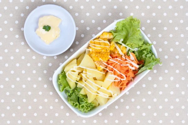 Plat de salade comme pomme de terre en streaming, maïs sucré, laitue et carotte hachée servi avec de la crème de salade remplie sur gris . — Photo