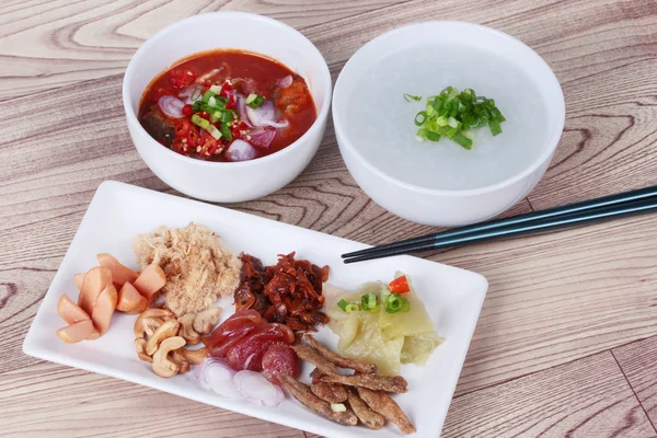 Gruau de riz et plat d'accompagnement sur bois. (Porc râpé séché, saucisse chinoise, poisson croustillant, saucisse, palourdes frites, oignon rouge tranché, chou chinois mariné, salade de sardines épicée et échalotes  ) — Photo