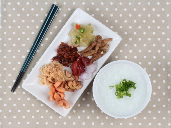 Pirinç gruel ve garnitür kahverengi napery üzerinde. (Kurutulmuş rendelenmiş domuz eti, Çin sosis, gevrek balık, sosis, kızarmış bebek istiridye, dilimlenmiş kırmızı soğan, turşu Çin lahanası, Baharatlı sardalya salatası ve arpacık )